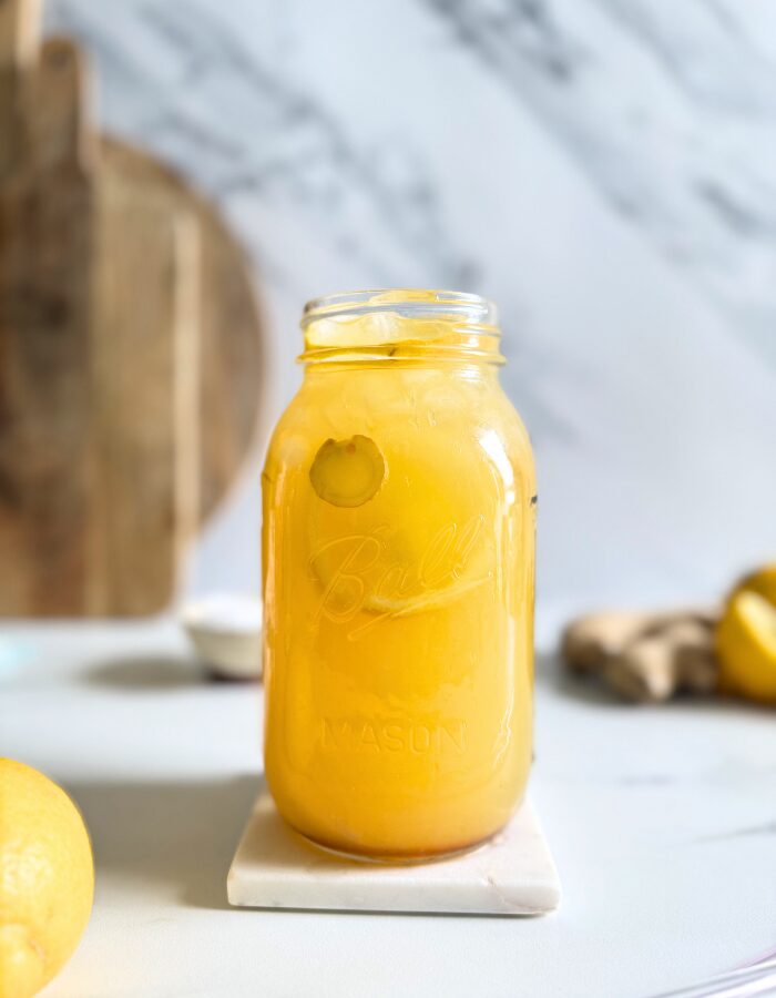 hand holding a jug of natures gatorade on a marble coaster, straws on front, lemons and ginger in the back with a bowl of salt