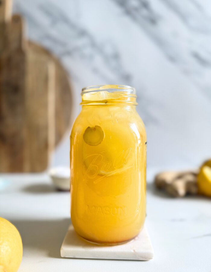 close up hand holding a jug of natures gatorade on a marble coaster, straws on front, lemons and ginger in the back with a bowl of salt