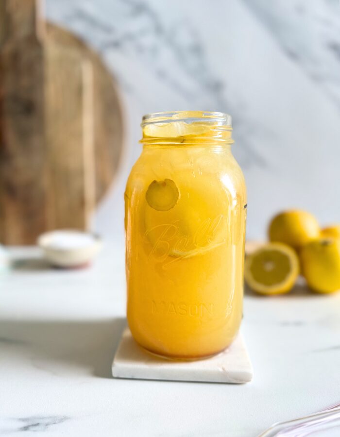 jug of natures gatorade on a marble coaster, straws on front, lemons and ginger in the back with a bowl of salt
