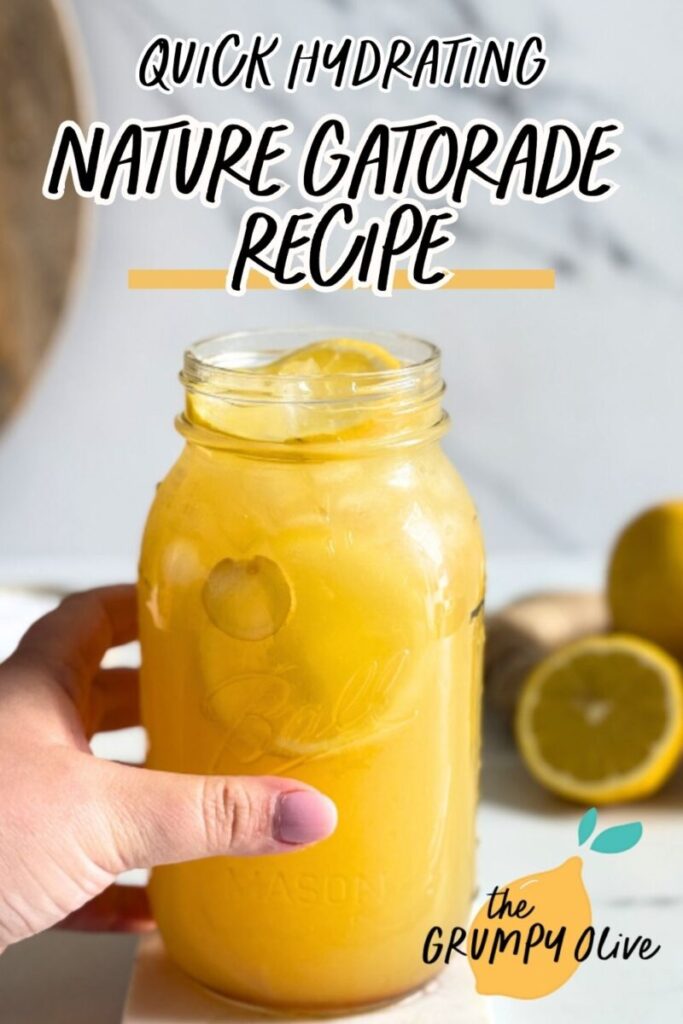 pin image hand holding a jug of natures gatorade on a marble coaster, straws on front, lemons and ginger in the back with a bowl of salt