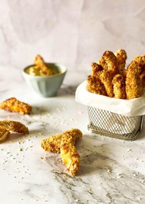 Home The Grumpy Olive NEW 35 chicken fries in a container with parchment paper on a marble background, more fries around and panko, behind a bowl with mayo