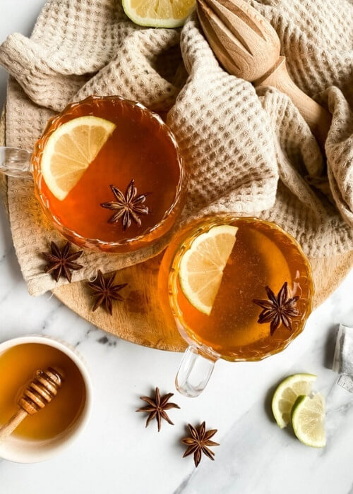 Easy Mocktail Recipes You Should Try 14 from top two cups of hot toddy mocktail with slices of lemon and star anise, over a wooden board and light brown tea towel, slices of lemons, star anise and honey around,