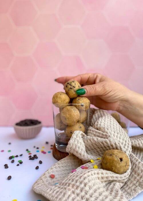 The Best No Bake Edible Cookie Dough Bites 4 cookie dough bites in a glass, napkin, chocolate chips on the side, a hand reaching for one