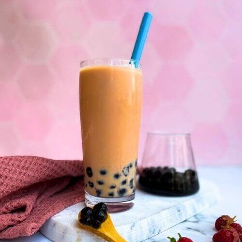 a strawberry milk tea on a marble tray with a glass of boba on pink background