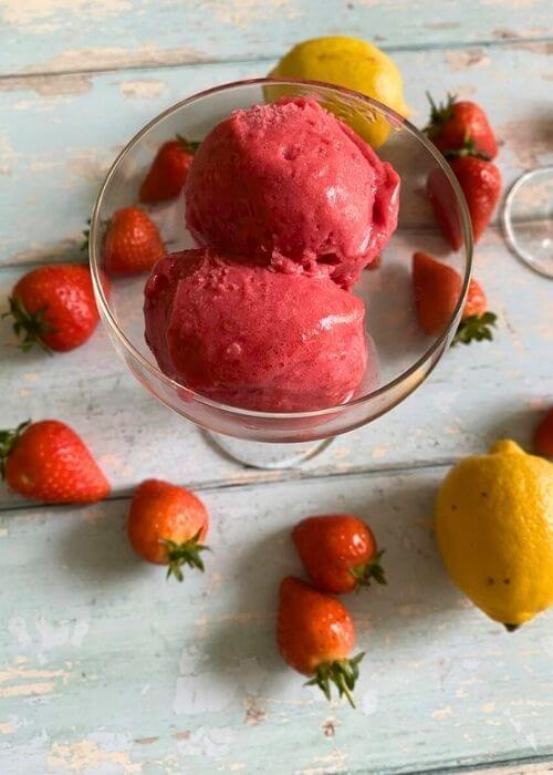 3 Ingredient Strawberry Sorbet Without Ice Cream Maker 2 strawberry sorbet no churn in a glass bowl, strawberries and lemons around on a light blue background
