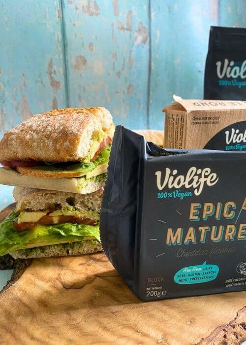 Violife Cheese Review From A Non-Vegan 5 three packs of violife cheese on a wooden board, beside a cheese sandwich, all on a wooden board, blue background