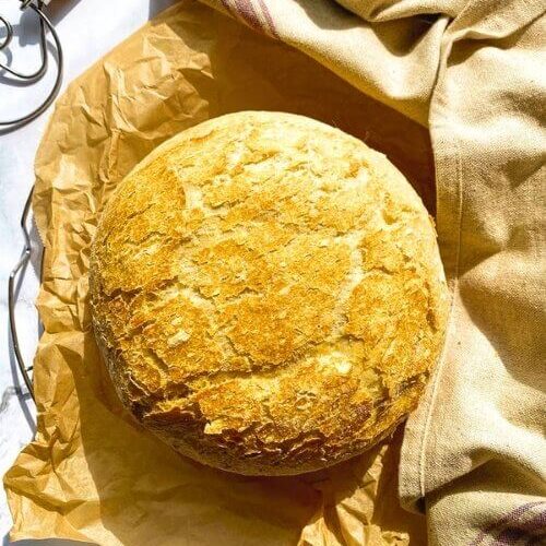 3 Minutes No Knead Bread Without Dutch Oven 4 no knead bread, under parchment paper, wire rack, towel and on the side a bread a dough whisk, on marble background