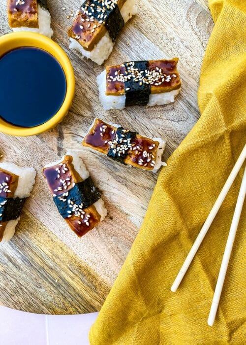 Super Delicious Tofu Nigiri With Garlic Soy Sauce 4 tofu nigiri around a bowl of soy sauce, on a wooden board and yellow towel, chopsticks on side