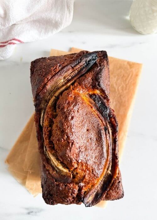 from top 4 ingredient banana bread, on marble background, a glass of milk and towel on the side