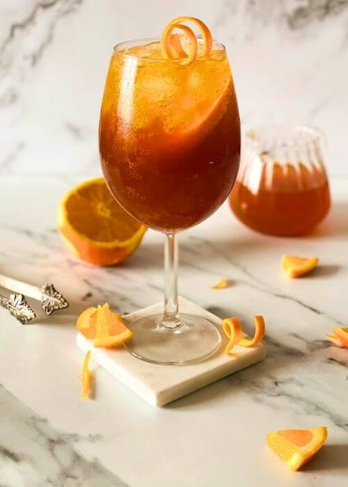 Easy Mocktail Recipes You Should Try 3 close up, aperol spritz mocktail, marble background, ice tongues and slices of orange around and a jug of liquid