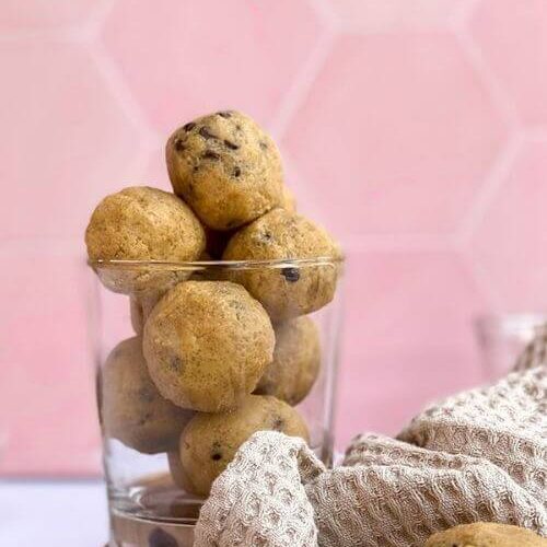 The Best No Bake Edible Cookie Dough Bites 5 close up cookie dough bites in a glass, choc chips and towel on the side, pin background
