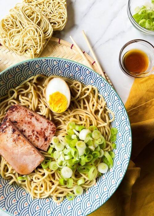 The Ponyo Ramen Recipe You Can't Miss Out On Because It's Delicious 7 a bowl of ponyo ramen with noodles, spring onions, ham and egg. under a yellow towel, chopsticks, bowls with ingredients on a marble background