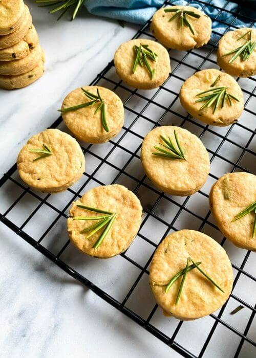 Most Delicious Savory Shortbread With Parmesan And Rosemary, 4 close up - savory shortbread cookies with rosemary on top, on a cooling rack, under a blue towel, more cookies around, on a marble background