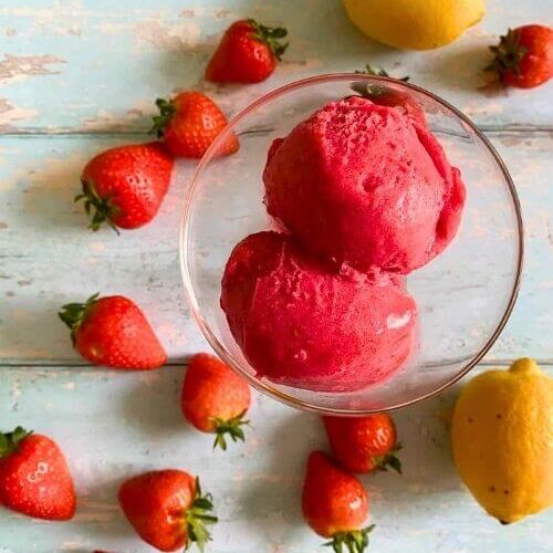 3 Ingredient Strawberry Sorbet Without Ice Cream Maker 3 from top strawberry sorbet no churn in a glass bowl, strawberries and lemons around on a light blue background