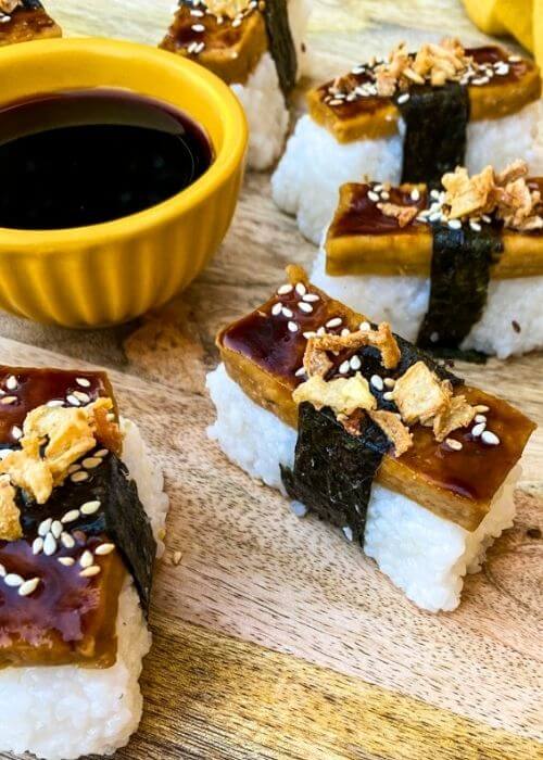Super Delicious Tofu Nigiri With Garlic Soy Sauce 3 close up of tofu nigiri around a bowl of soy sauce, on a wooden board and yellow towel