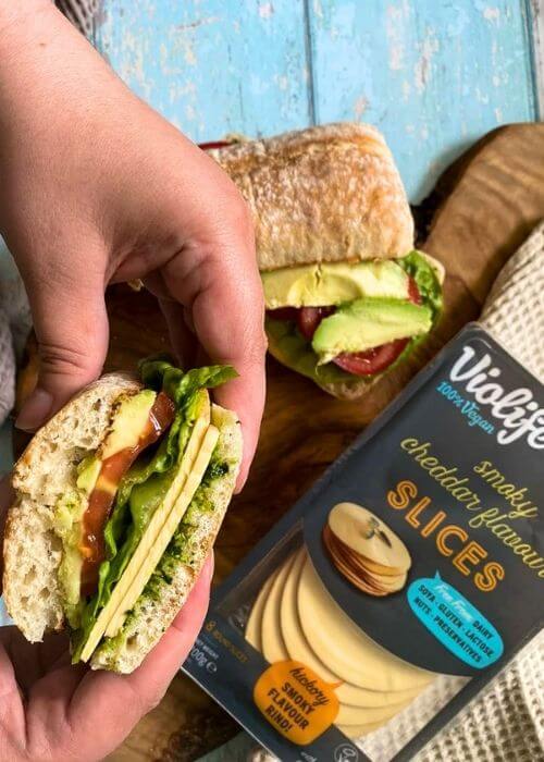 Violife Cheese Review From A Non-Vegan 3 from top, two hands holding a cheese sandwich, pack of violife cheese review, on a wooden board and wooden background, towel on the side