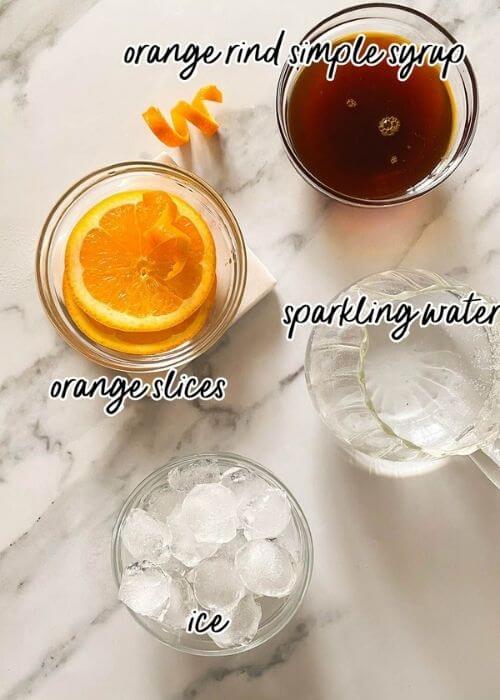 Super Aperol Spritz Mocktail, Just Like The Real One 2 ingredients for aperol spritz mocktail in bowls on a marble background
