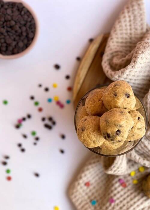 The Best No Bake Edible Cookie Dough Bites 2 from above, chocolate chips, cookie dough bites in a glass on top op towel and wooden board