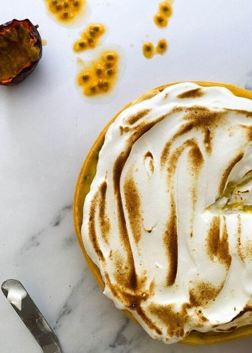 Delicious Passion Fruit Meringue Pie 4 close up passion fruit meringue pie on a marble background, passion fruit and seeds on the side, spatula with meringue on the side
