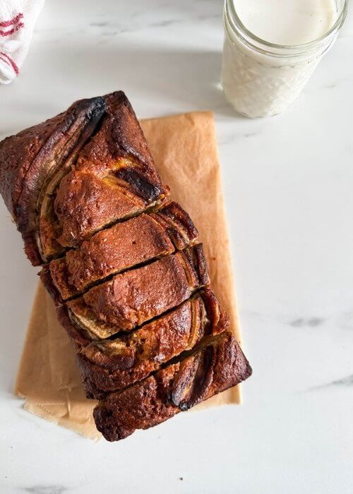 4 ingredient banana bread sliced, on marble backround, a glass of milk and towel on the side