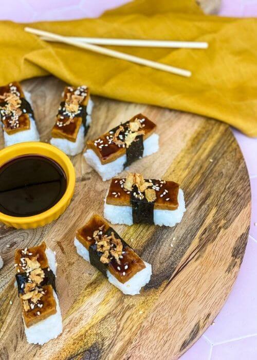 Super Delicious Tofu Nigiri With Garlic Soy Sauce 1 tofu nigiri around a bowl of soy sauce, on a wooden board and yellow towel
