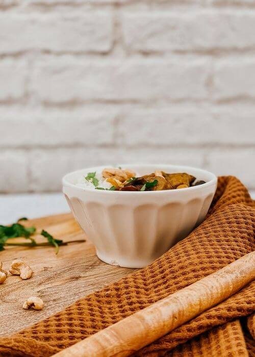 Vegan Mushroom Korma, The #1 Best Recipe 3 mushroom korma in a bowl, a napkin, wooden board and spoon, parsley and cashews on the side