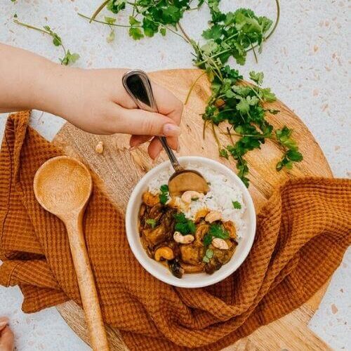 Vegan Mushroom Korma, The #1 Best Recipe 5 mushroom korma in a bowl, a napkin, wooden board and spoon, parsley on the side, hand with a spoon