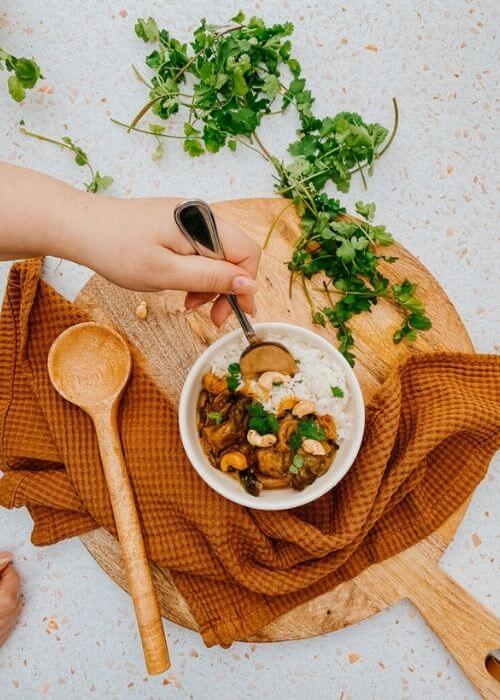mushroom korma in a bowl, a napkin, wooden board and spoon, parsley on the side, hand with a spoon
