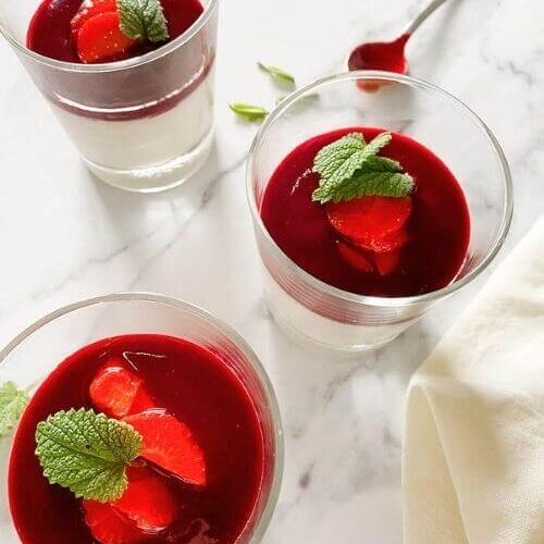 The Best Vegan Panna Cotta 6 vegan panna cotta in glasses on a marble background, a spoon and mint leaves on the side, towel on the side