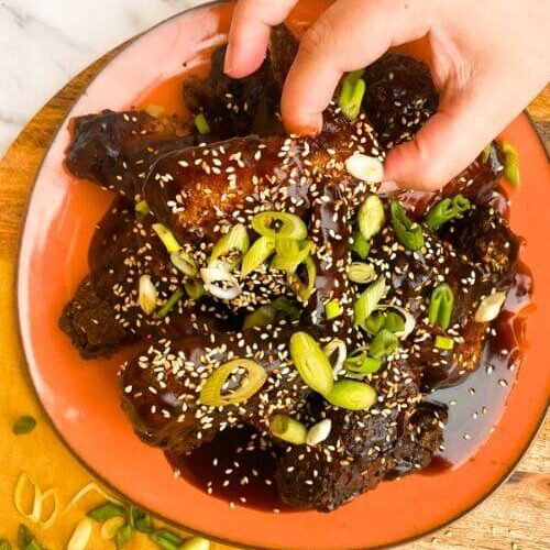 Best Crispy Fried Soy Garlic Chicken Wings Recipe 5 from top - hand reaching soy garlic chicken wings on a plate, on a wooden board and yellow towel