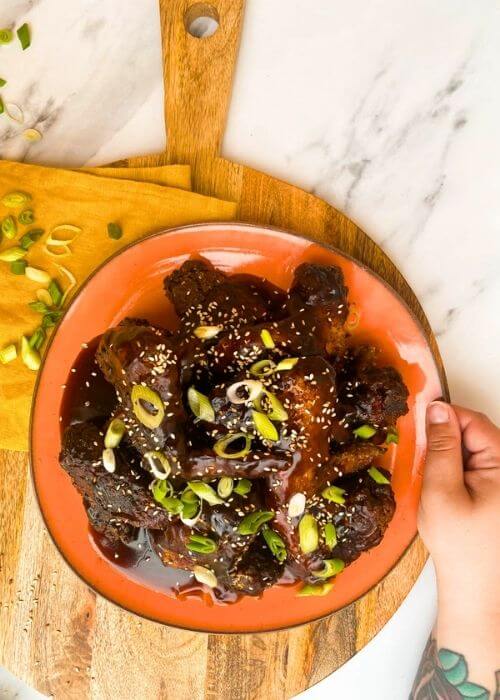 Best Crispy Fried Soy Garlic Chicken Wings Recipe 3 hand holding a soy garlic chicken wings on a plate, on a wooden board and yellow towel