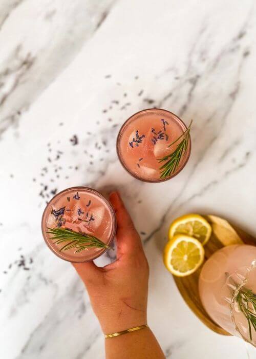 Lavender Lemonade Cocktail 20 Minutes Delicious Drink 3 hand reaching for a glass of lavender cocktail, more cocktail mix on the side, marble background