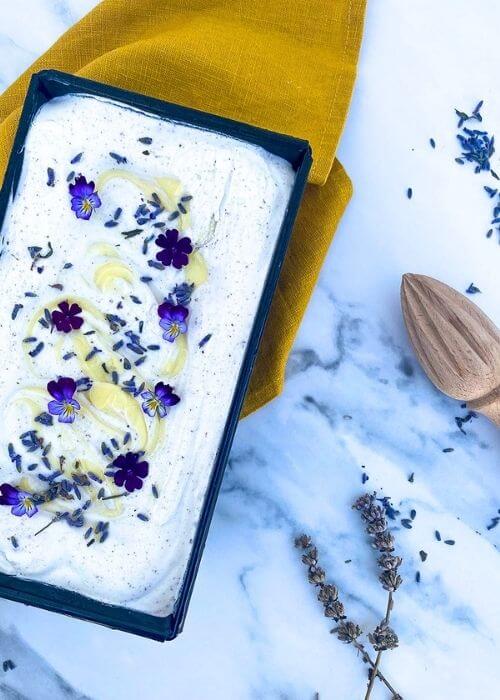 The Best Lavender Lemon Ice Cream Recipe To Try Immediately 3 from top - lavender lemon ice cream in a loaf pan, a yellow towel under, lemon, lemon squeezer and lavender buds around, on a marble background