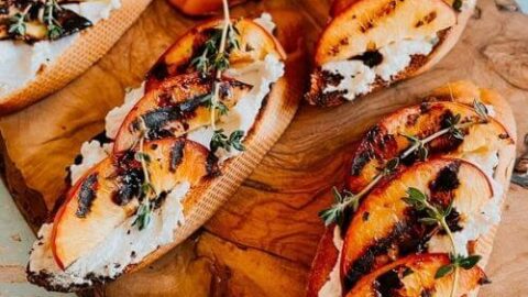peach and ricotta crostini on a wooden board, more ricotta on the background