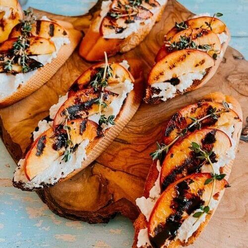 peach and ricotta crostini on a wooden board, more ricotta on the background