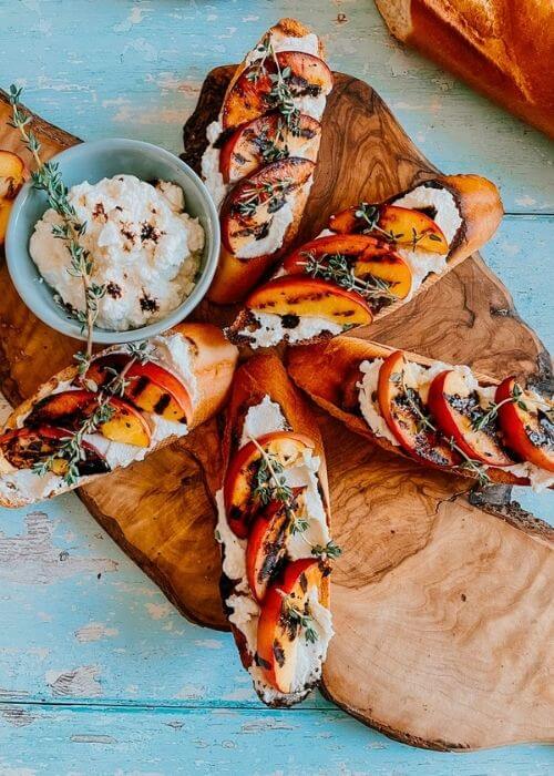 Delicious Peach Ricotta Crostini with Thyme and Balsamic 2 peach and ricotta crostini on a wooden board, more ricotta on the background from above