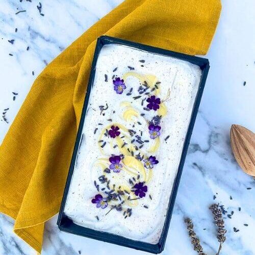 The Best Lavender Lemon Ice Cream Recipe To Try Immediately 5 from top - lavender lemon ice cream in a loaf pan, a yellow towel under, lemon, lemon squeezer and lavender buds around, on a marble background
