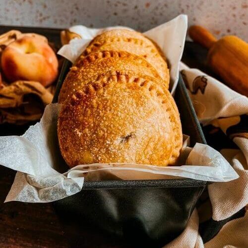 Super Easy Peach Hand Pies With a Fresh Basil Filling 5 peach hand pies in a tin, peaches on the left and a rolling pin on the right