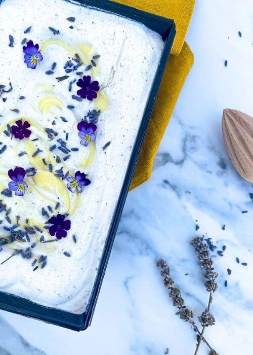 The Best Lavender Lemon Ice Cream Recipe To Try Immediately 2 close up detail - from top - lavender lemon ice cream in a loaf pan, a yellow towel under, lemon squeezer and lavender buds around, on a marble background