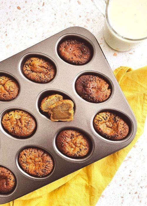 Delicious Matcha Mochi Muffins 2 matcha mochi muffins in a tin on a yellow napkin, a hand squeezing a muffin, from above