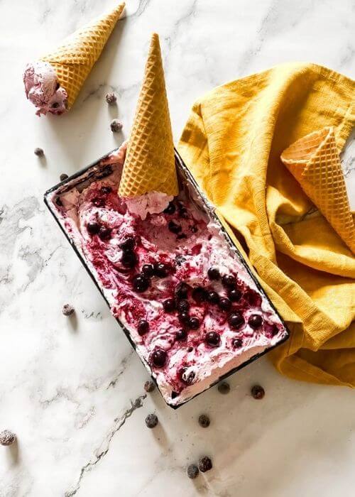 Blackcurrant Ice Cream: The Delicious Summer Recipe 3 blackcurrant ice cream in a tin with ice cream cones around, blackcurrants around