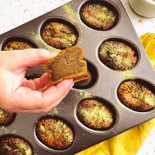 Delicious Matcha Mochi Muffins 5 matcha mochi muffins in a tin on a yellow napkin, a hand holding one
