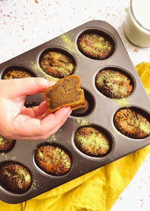 matcha mochi muffins in a tin on a yellow napkin, a hand holding one